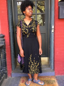 Krystal stands at her front door wearing a   tonle dress that is black and designed with golden willow leaves